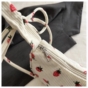 Detail of strawberry embroidery on white corduroy bag with silver zipper closure