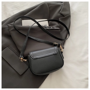 Detail of black lychee texture saddle bag with gold hardware on a gray blazer