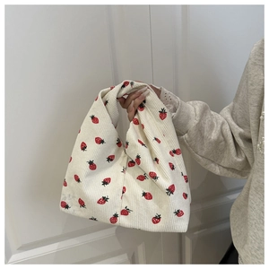 Détail du sac à main en velours côtelé blanc avec motifs fraises rouges et poignée unique