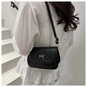 Detail of a black square crossbody bag with golden bow buckle worn by a model