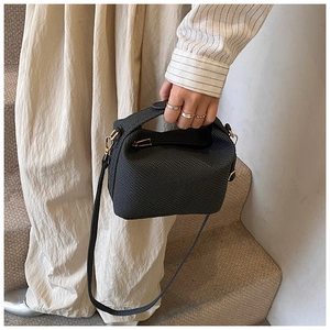 Close-up of a black waffle texture crossbody bag with gold hardware held by a model