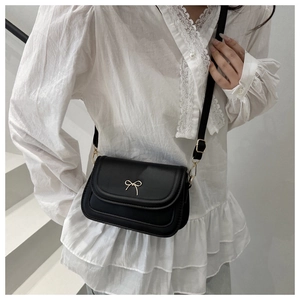 Detail of black textured PU leather bag with golden bow hardware on white lace top