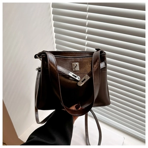 Detail of dark coffee polished leather handbag with metal turn-lock and leather straps