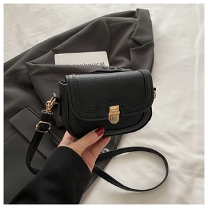 Close-up of black litchi grain leather texture and golden metal buckle on crossbody bag