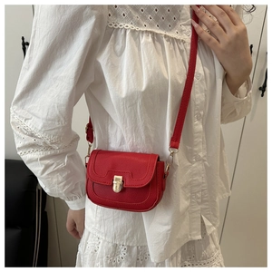 Close-up of red lychee pattern saddle bag with gold buckle on a white lace shirt
