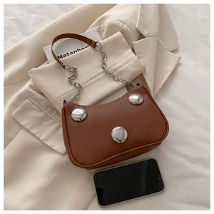 Detail view of crescent bag with large silver studs and chain strap on beige suit