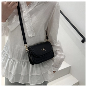 Side view of a vintage black crossbody square bag with a golden bow on white stairs