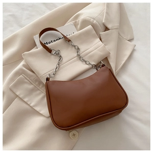 Detail of brown crescent bag with silver chain strap on a beige suit background