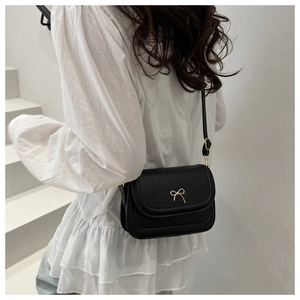 Detail of a black square crossbody bag featuring a golden bow buckle on the back of a model