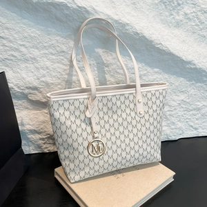 Minimalist beige tote bag with M-pattern print and gold metal charm on stone background