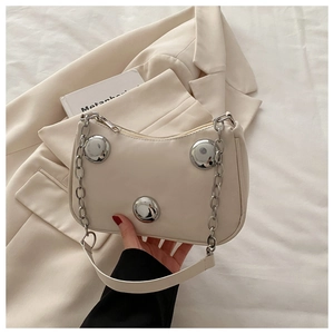 Detail view of cream crescent bag featuring bold silver studs and metallic chain strap