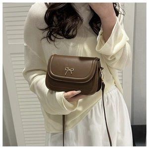 Detail of vintage brown crossbody bag with gold bow clasp and sleek matte leather texture
