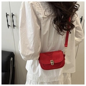 Detail of red pebbled leather crossbody bag with golden metal buckle clasp on model