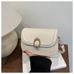Close-up of cream saddle bag with gold U-shaped buckle and fine stitching details