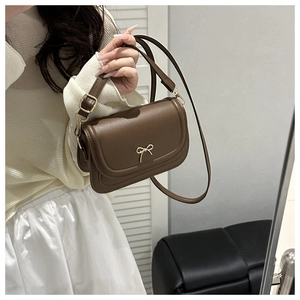 Detail of a brown leather crossbody bag with an elegant golden bow buckle