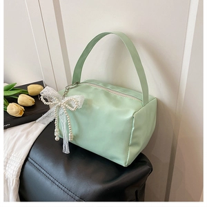 Detail of mint green small square bag featuring a pearl lace bow charm and soft matte leather