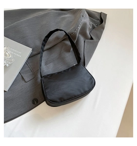 Flat lay of minimalist black nylon underarm bag with silk finish and professional props