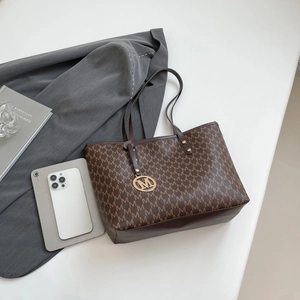 Classic brown tote bag with M letter pattern, metal tag and grey blazer background