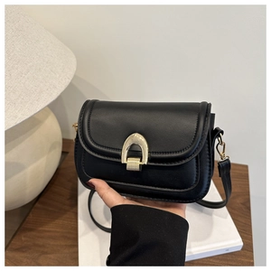 Detail of a black vintage saddle bag with a golden horseshoe buckle and leather strap