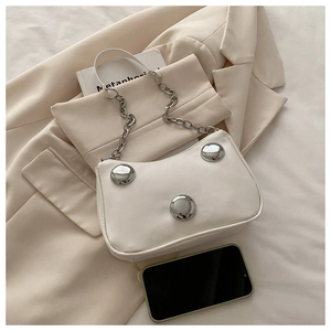 Detail of white crescent bag featuring large silver studs and chain strap on neutral decor