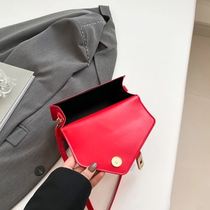 Minimalist red leather crossbody bag with gold magnetic buckle on a white desk