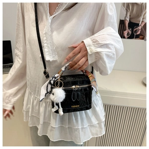 Detail of glossy black bucket bag with silk scarf handle and plush doll pendant detail