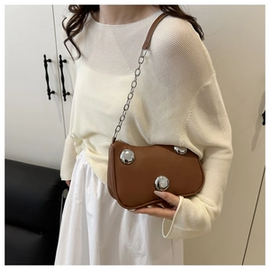 Brown crescent bag with silver spheres shown on a model in a minimalist setting