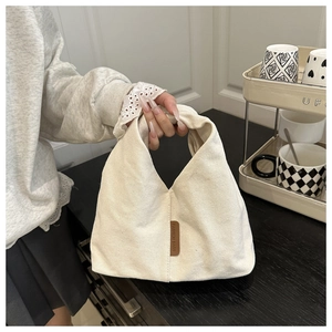 Gros plan d'un sac à main en toile blanc cassé avec écusson en cuir marron tenu