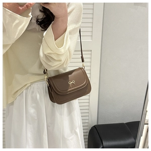 Brown leather crossbody bag with a decorative golden bow clasp shown in a mirror selfie