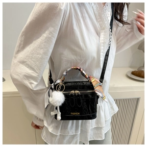 Detail of black leather crossbody bag with silk scarf handle and plush ball charm decoration
