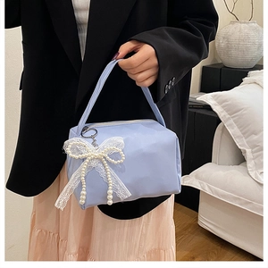 Detail of light blue handbag with white lace bow and pearl pendant in lifestyle setting