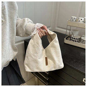 Détail d'un sac à nœud en toile crème avec étiquette en cuir marron et anse