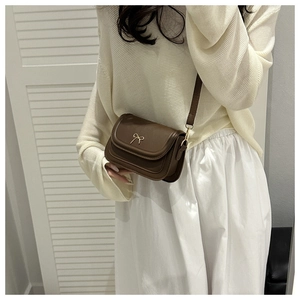 Close-up of a dark brown crossbody bag featuring a delicate gold bow metal fastener