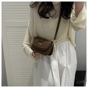 Detail of a brown leather crossbody bag with a golden bow metal accessory clasp