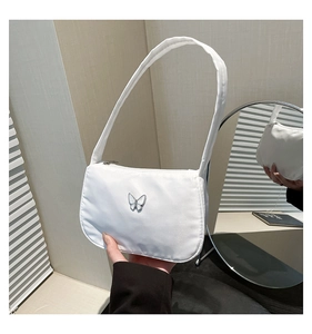 Close-up of white shoulder bag with silver butterfly emblem and smooth nylon texture