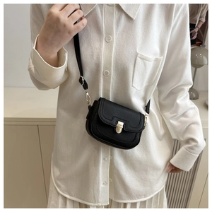 Close-up of black lychee-textured crossbody bag with gold clasp on a white shirt