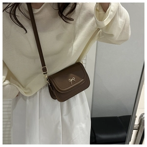 Mirror selfie showing the brown matte leather saddle bag with a golden bow buckle