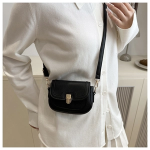 Gros plan d'un sac besace en cuir grainé noir avec boucle dorée sur tenue blanche
