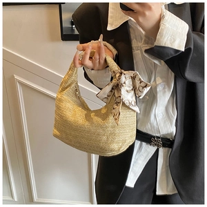 Detail einer beigen Strohtasche mit einem dekorativen Seidenschal am oberen Tragegriff
