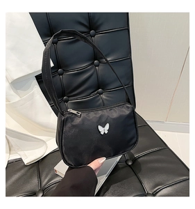 Detail of black satin shoulder bag featuring a white butterfly ornament on a textured seat