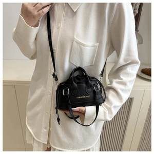 Close-up of black lychee-grain leather crossbody bag worn by model with gold lettering