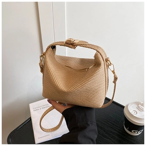 Detailed close-up of natural straw-woven small square bag with golden metal hardware