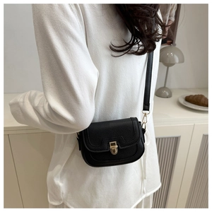 Chic black crossbody bag with gold buckle worn by model in minimalist home setting