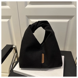 Détail d'un sac à main en toile noire avec poignée nouée et écusson logo en cuir