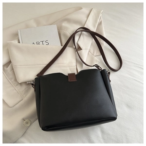Detail view of black leather bucket bag with brown straps on white blazer and arts book