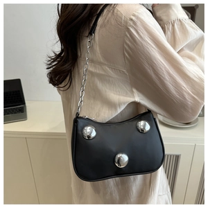 Detail of a chic black shoulder bag with three oversized silver spheres and metal chain strap