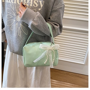 Close-up of mint green handbag featuring a white lace bow and pearl chain details