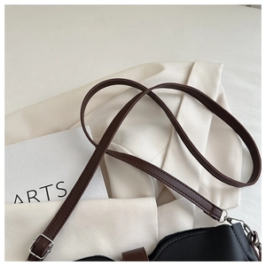Detail of black bucket bag featuring wavy edge design and brown adjustable strap with silver hook