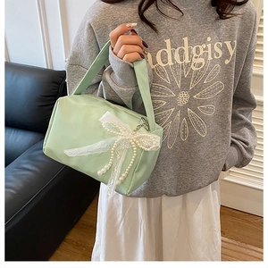 Detail of mint green handbag featuring a delicate white lace and pearl bow charm accessory
