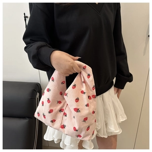 Détail d'un sac à main en velours côtelé rose à motif fraises tenu par un mannequin